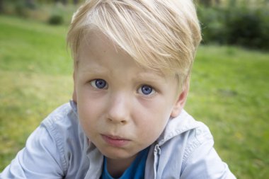 Üzgün çocuk doğanın yeşil çimenlerin üzerinde oturuyor.