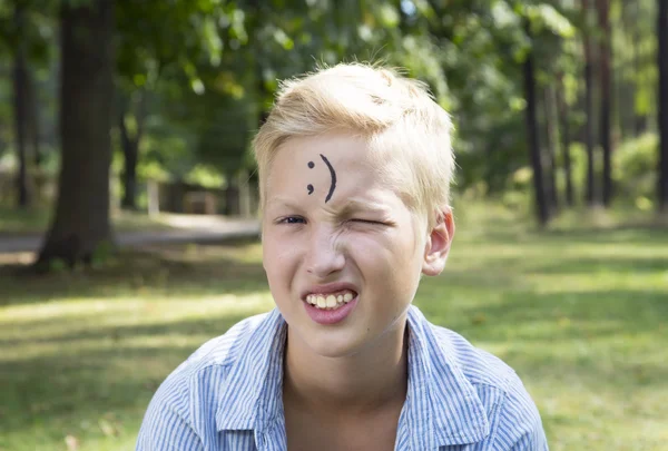 Winking boy est assis sur l'herbe verte dans la forêt. Concept de heureux tu — Photo