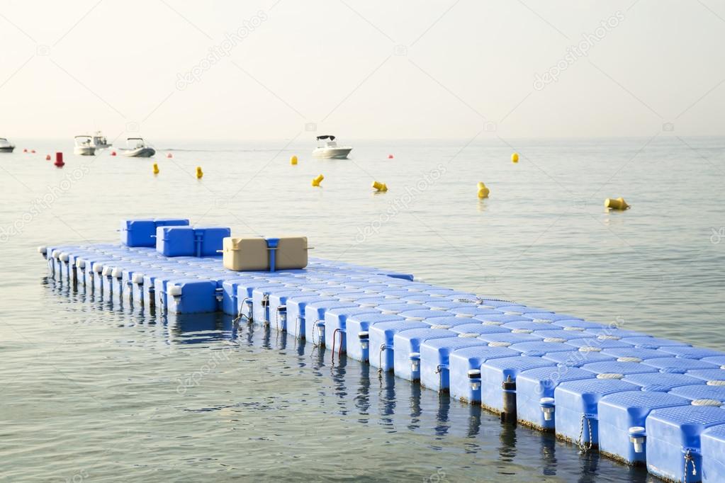 Plastic blue jetty in the empty sea against blue sky.