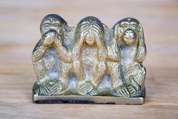 Brass statue of three monkeys isolated on wooden surface.