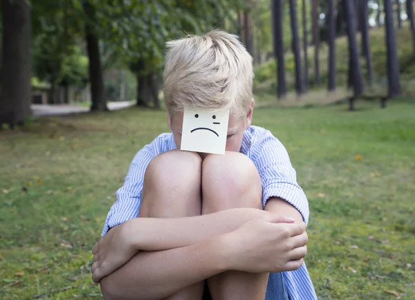 Gråtande pojken sitter på grönt gräs i skogen. Begreppet sorglig tanke — Stockfoto