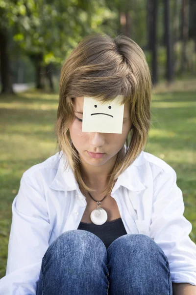 Sad girl sits on green grass in forest. On the forehead shows (d — Stock Photo, Image