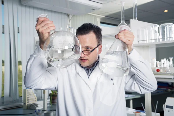 Asistente de laboratorio mirando en una botella con líquido —  Fotos de Stock