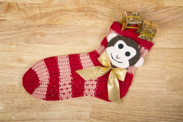 Chaussette rouge de Noël avec singe et tous les cadeaux isolés sur la surface du bois . — Photo