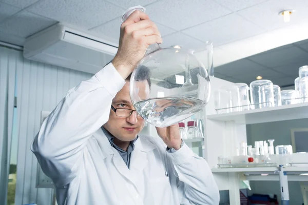 Assistente de laboratório olhando em uma garrafa com líquido — Fotografia de Stock