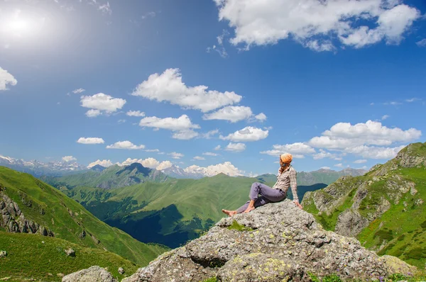 Kobieta siedzi na krawędzi klifu i patrzy na dolinę słońca i góry. — Zdjęcie stockowe