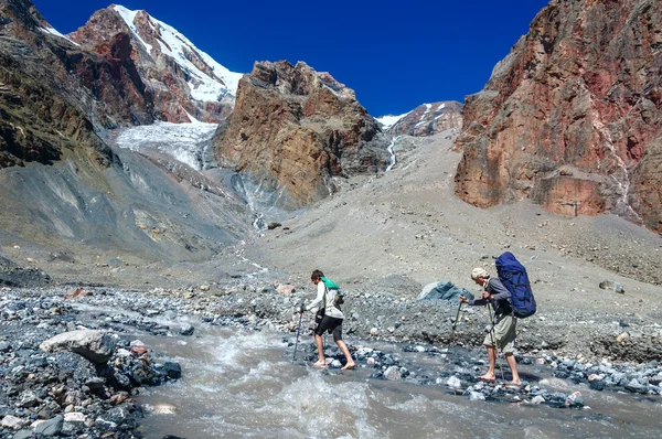 Two hikers crossing mountain river — Stock Photo, Image