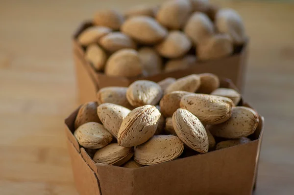 Almonds on table in hard shells, group of dry ripened fruits in brown cardboard boxes, harvested healthy food ingredients ready for baking and cooking