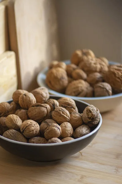 Walnuts on table in hard shells, group of dry ripened fruits in black and blue bowl, harvested healthy food ingredients ready for baking and cooking