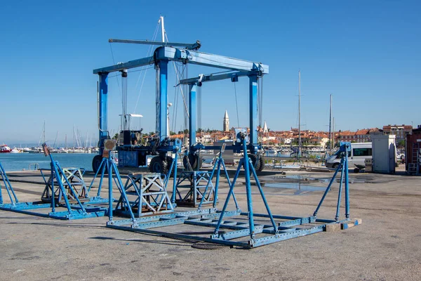 Izola, SLOVENIA - 13 Eylül 2019: Gemiler ve tarihi şehir merkezi için arka planda kulesi olan marina mavi kaldırma ekipmanlarının görüntüsü