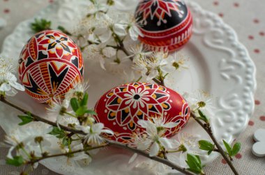 Ev yapımı el yapımı Paskalya yumurtaları beyaz tabakta benekli masa örtüsü ile süslenmiş erik rengi, siyah dikenli beyaz çiçek dalları, tahta çiçekler, yeşil yapraklar.