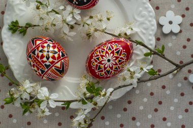 Ev yapımı el yapımı Paskalya yumurtaları beyaz tabakta benekli masa örtüsü ile süslenmiş erik rengi, siyah dikenli beyaz çiçek dalları, tahta çiçekler, yeşil yapraklar.