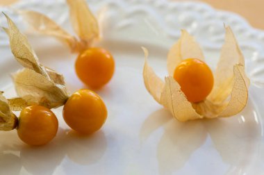 Physalis Peruviana yenilebilir lezzetli physalis turuncu meyveler kuru kabuklarda beyaz tabakta yayılmış kağıt üzerinde