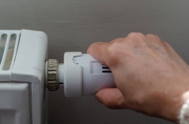 Kadın evde tasarruf yapmak için radyatör vanasını kapatıyor.