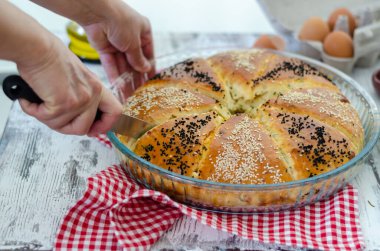 Geleneksel mayalanmış ekmek ve cam tepside susam tohumu. Kadın ekmeği kesiyor..