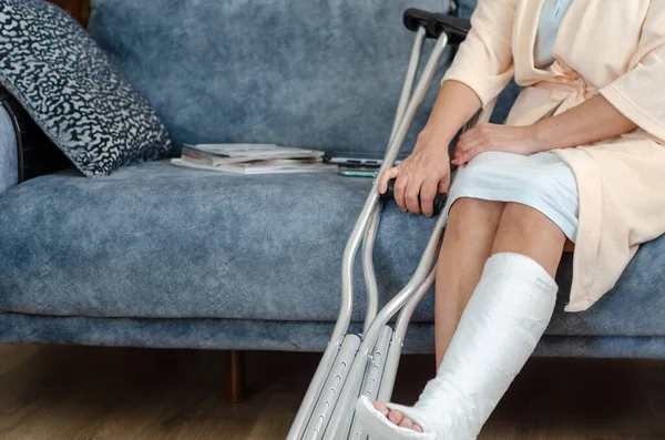 The middle aged woman with broken leg .She  is sitting on the sofa