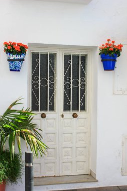 Güney İspanya 'da tipik bir beyaz köy olan Mijas Pueblo' da minimalist ahşap ön kapı, beyaz duvar ve yeşil bitkilerle dolu kaplar..