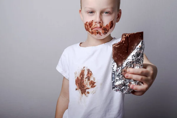 upset boy in dirty clothes holding a chocolate bar. The concept of cleaning stains on clothes. . High quality photo