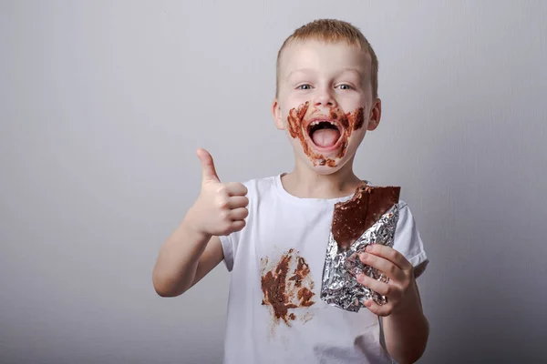 boy eating chocolate with a stain on clothes. Stains on a white chocolate T-shirt