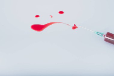 Mavi arka plandaki şırıngadan bir damla kan. Kanlı hüzünlü ifade 