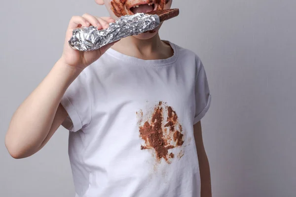 Jongen eet chocolade met een vlek op kleding Het concept van het reinigen van vlekken op kleding. — Stockfoto