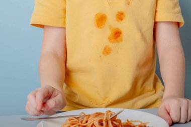 Sarı tişörtte ketçap lekeleri var. Günlük hayat, temizlik ve temizlik için kirli bir leke. Mavi arkaplanda izole edilmiş
