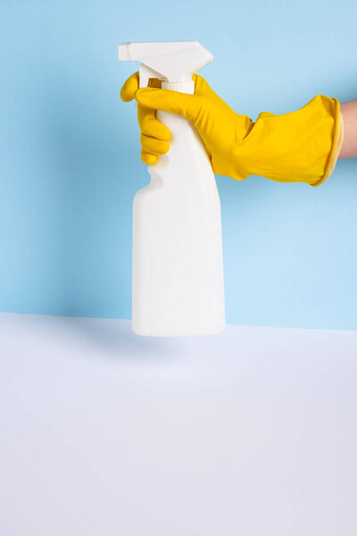 Женщина рука в желтой резиновой защитной перчатке держа триггер белый пластиковый баллончик один синий фон. обычная или обычная уборка. пустое место для текста или логотипа. высокое качество фото