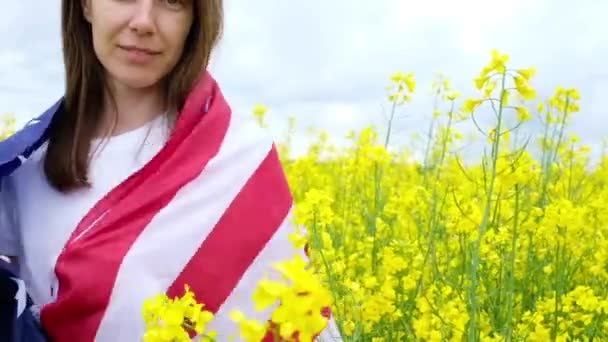 Ung flicka viftar den amerikanska flaggan i ett fält av gula blommor — Stockvideo