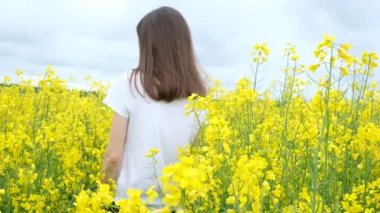 Sarı çiçeklerin arasında beyaz tişörtlü genç bir kadın.