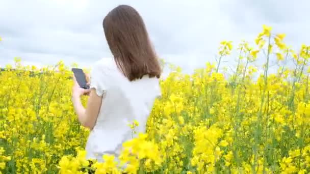 Mulher nova em uma camiseta branca entre um campo de flores amarelas — Vídeo de Stock