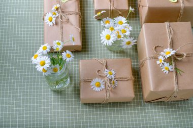 Kahverengi el işi kağıdıyla sarılmış ve doğal papatya çiçekleriyle süslenmiş hediye kutuları. Üst manzara, düz yatak, metin için yer. Yüksek kalite fotoğraf