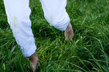 Beyaz pantolonla çimenlerde koşan çıplak ayaklı kadın. Günlük hayat, temizlik ve temizlik için kirli bir leke. Yüksek kalite fotoğraf