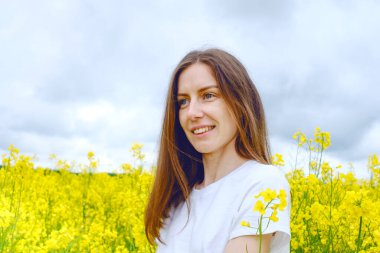 Makyajsız, sarı çiçeklerin arasındaki bir tarlada geniş bir gülümsemesi olan güzel bir kız. Yüksek kalite fotoğraf