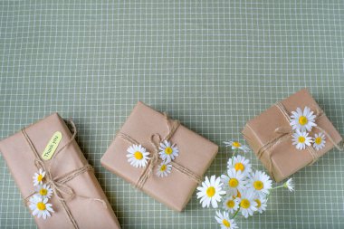 Kahverengi el işi kağıdıyla sarılmış ve doğal papatya çiçekleri ile süslenmiş bir eko hediye kutusu. Üst görünüm, düz görünüm, metin için yer.