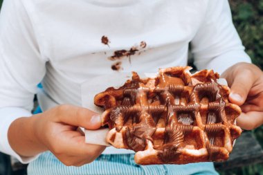 Children's hands holding a Belgian waffle with chocolate topping. close up . High quality photo clipart