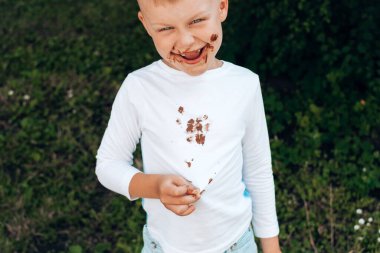 Beyaz elbiselerinde çikolata lekeleri, yüzünde kir olan bir çocuk. Yüksek kalite fotoğraf
