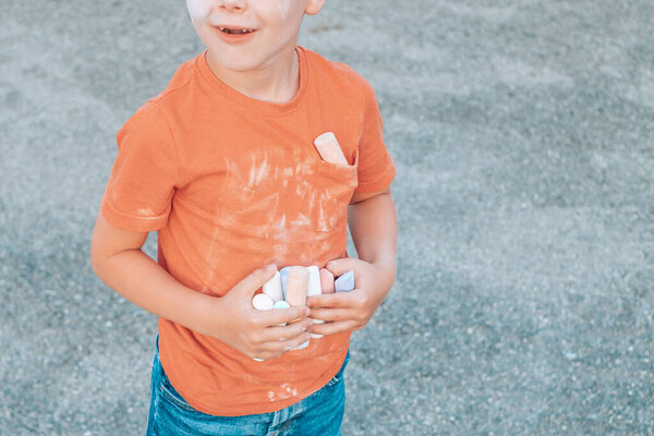 Child holding colored chalk in his hands and dirty t-shirt in front. High quality photo