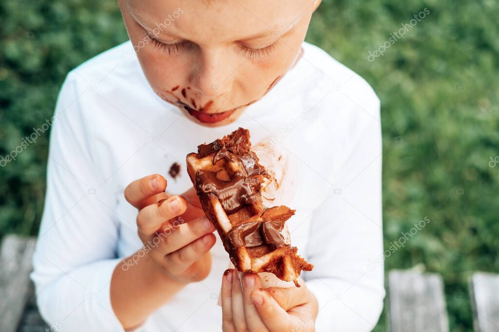The child eating a Belgian waffle with a chocolate topping.top view. daily life dirty stain for wash and clean concept. High quality photo