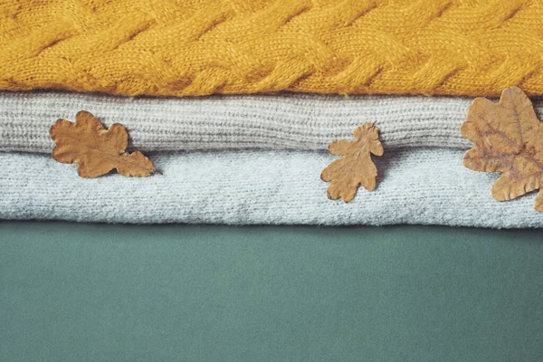 Eichengelbe Blätter auf dem Hintergrund eines Bündels herbstlich gestrickter Pullover. Recyclingkonzept für Kleidung. — Stockfoto