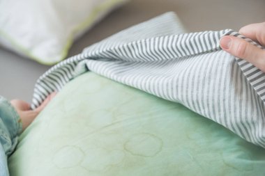 Kadın eller oturma odasında yastıktan yastık kılıfını kaldırıyor. Yeşil bir yastıkta kirli ter ya da tükürük lekeleri. Bilinçli evde bakım ve sürdürülebilir yaşam konsepti. Üst Manzara. Yüksek kalite fotoğraf