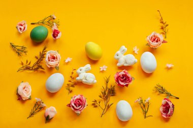 Paskalya tatili konsepti. Sarı arka planda el yapımı şirin yumurtalar, tavşan ve çiçekler. Düz konsept, üst görünüm. Metin için bir paskalya kartı ve yerin bir kopyası..
