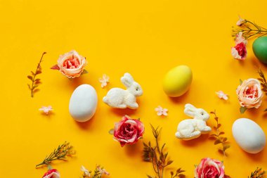 Paskalya tatili konsepti. Sarı arka planda el yapımı şirin yumurtalar, tavşan ve çiçekler. Düz konsept, üst görünüm. Metin için bir paskalya kartı ve yerin bir kopyası..