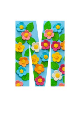 İngiliz alfabesinin M harfleri mavi arkaplandaki çiçeklerden kesilir. Çiçek deseni, mağazalar için doku, satışlar, web siteleri, kartpostallar ve bayram kutlamaları..