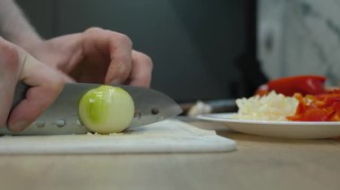 Bir şefin elleri, renkli sebzelerle çevrili bir tahtanın üzerinde ustalıkla soğan doğruyor. Yemek dersleri ve yemek hazırlama videoları için mükemmel.