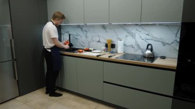 Önlüklü bir ev aşçısı yemek için malzemeler hazırlar. Mutfak sahnesinde aşçı lavaboda biber yıkarken görülüyor.