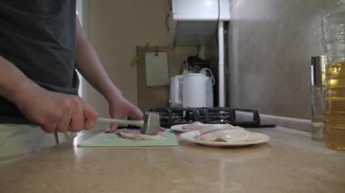 Taze domuz dilimli kahvaltıyı hazırlayan kişi, rahat ev ortamında sobanın yanındaki sıcak mutfakta çiğ eti ustalıkla keser.