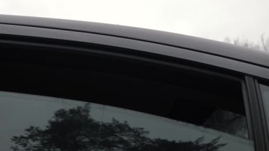 Yağmurlu bir arabanın camındaki ağaçların yansıması. Arabaların arka camları yükselir ve düşer, bulutlu gökyüzüne karşı ağaçları yansıtır.