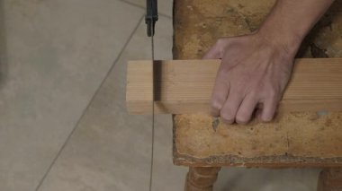 Eller tahta testeresi, ince meşe bıçağı aşınmış taburede talaş, sabit tutuş ve hassas hareketler, tozlu atölye zemini, sıcak doğal ışık aydınlatma dokusu ve doğaçlama tekniği.