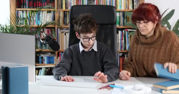 可爱的男孩和妈妈在家做作业 妈妈帮儿子 教如何做作业 概念教育 男中学生被隔离 戴眼镜的有爱心的母亲帮助男孩在家里的电脑上做作业 — 图库视频影像