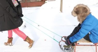 Anne oğlunu kızağa çekiyor, anne oğlunu kızakta otururken çekiyor.